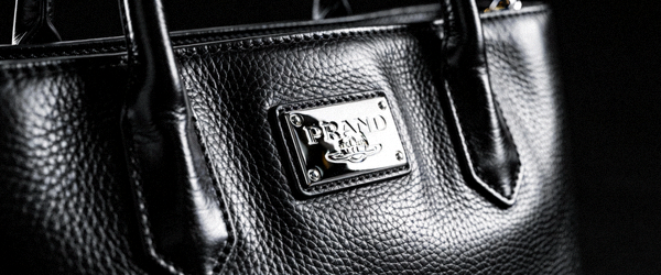 奢侈品黑色小牛皮托特包高清侧面实拍，突出皮革光泽感和金属logo铭牌