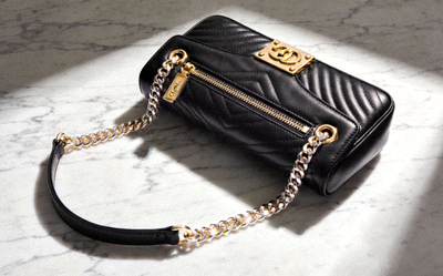 Luxury black leather replica shoulder bag with gold-tone hardware and chain strap on a marble surface