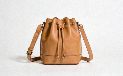 Minimalist tan leather bucket bag with a drawstring closure and adjustable strap